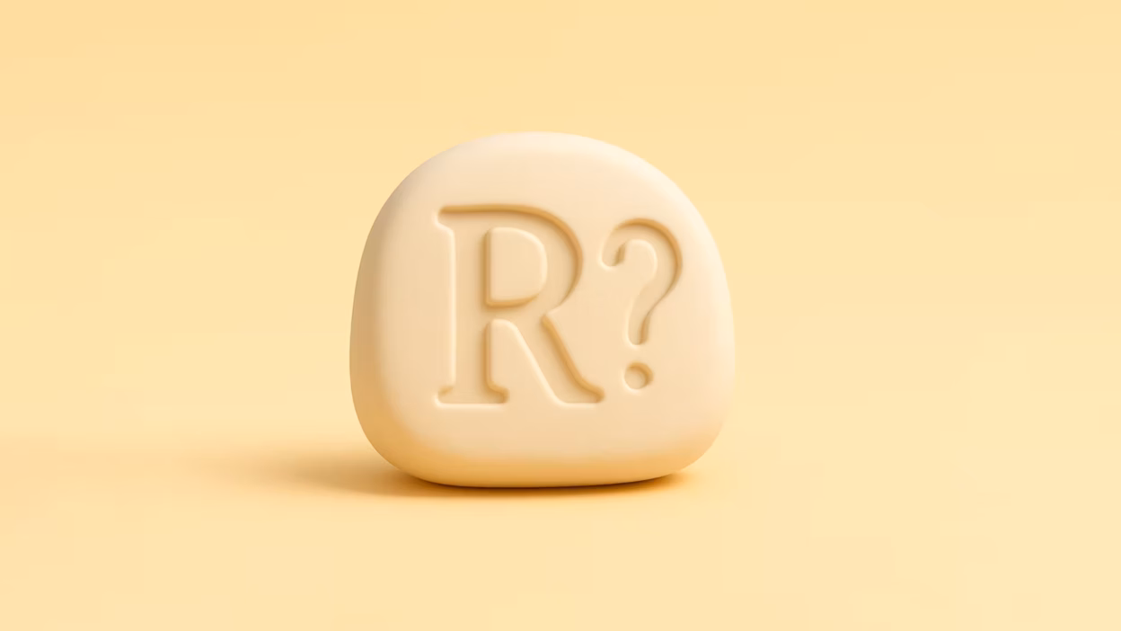 Engraved "R?" on a smooth cream 3D stone, pale yellow backdrop.